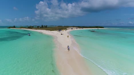 Drone-Disparó-A-Dolly-Fuera-De-Un-Banco-De-Arena-Tropical-Con-Personas-Paradas-En-Una-Playa-Caribeña-De-Arena-Blanca