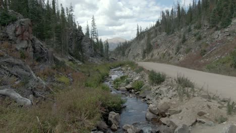 dolly shot of stream next to dirt road in the mountains of colorado in late summer