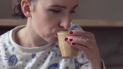 young beautiful girl drinking flat white coffee, picking up glass from a wooden table