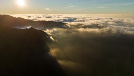 sunrise over mountain peaks with clouds below, golden light, aerial view