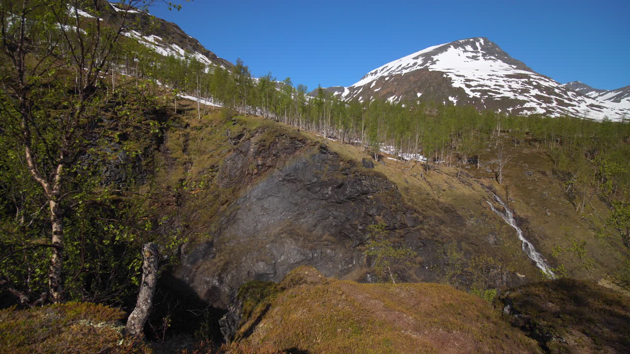 Aerial, pan drone shot of a canyon and a stream,  snowy mountain peaks in the background, sunny, summer day, in the Lyngen alps, North Norway
