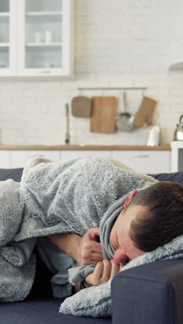 young man trembling from fever. sick man lying on couch at home and covering with warm blanket over the head. vertical video