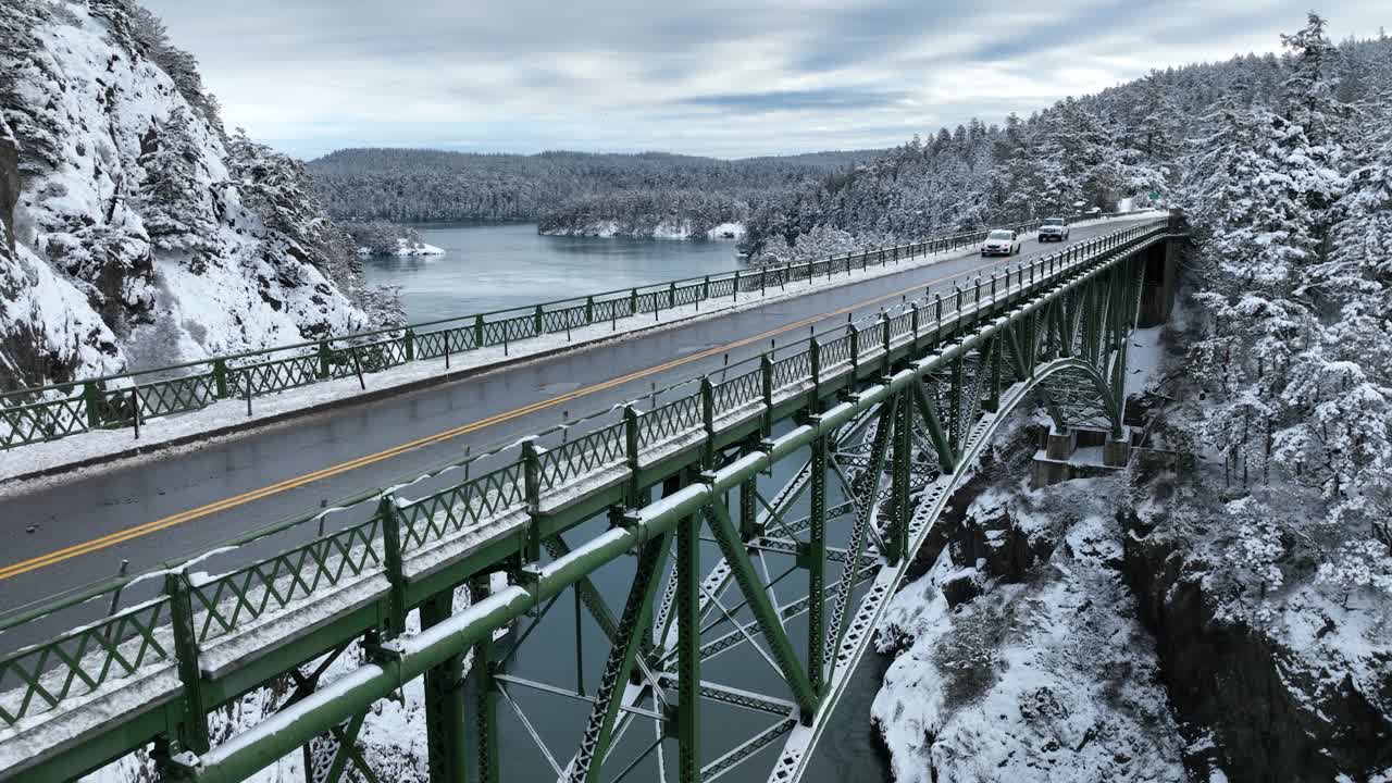 사방에 눈이 내리는 다리를 가로 질러 운전하는 자동차의 상승 공중 샷