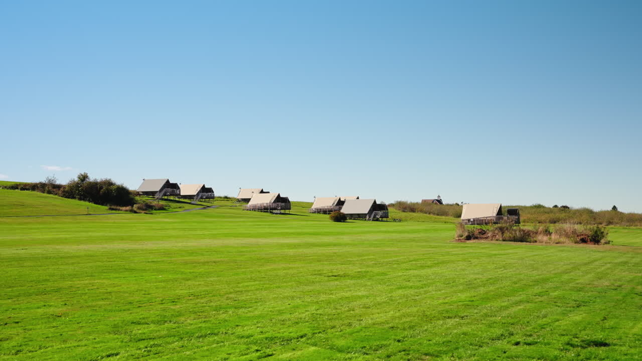 Panoramic view of green field rural landscape. Bright blue sky, wooden houses in the distance.