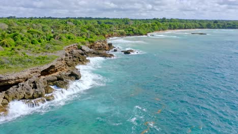 aerial shot of beautiful rocky coastline with waves of caribbean sea and tropical greenery in background