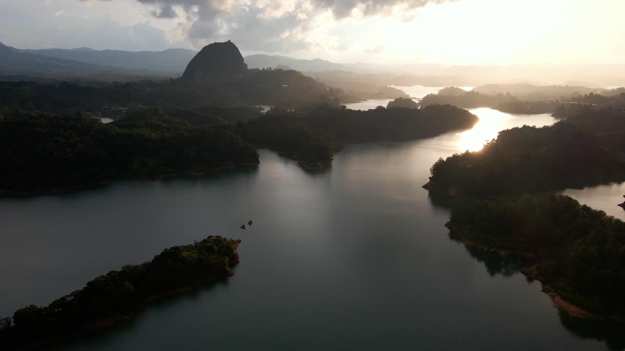 Aerial ascend of Guatapé Rock offset at sunrise, highlighting the contrast of water and tropical green terrain