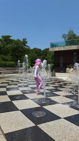 a happy 5-year-old girl in a swimsuit plays and splashes in a ground fountain at a public park in south korea, a fun way for children to cool off and beat the heat on a hot summer day