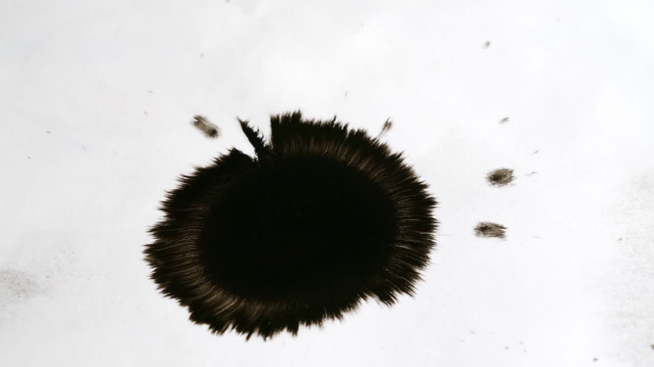 la tinta gotea sobre un papel blanco y se extiende rápidamente, formando un círculo irregular.