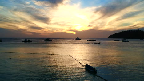 A-picturesque,-colourful-sunsets-with-reflection-falling-to-the-ocean-and-boats