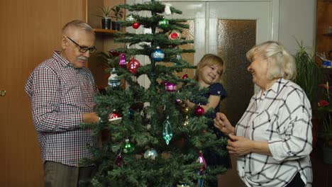 niña linda con abuelos mayores familia decorando árbol de navidad artificial en casa