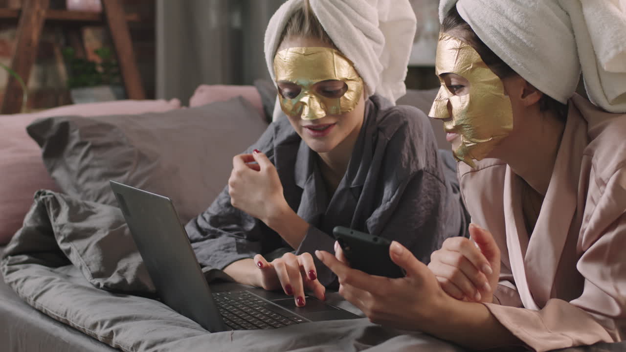 Girls In Sheet Masks Using Laptop In Bed