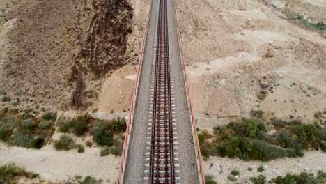 Toma-Aérea-De-Un-Dron-Lento-Hacia-Adelante-De-Un-Puente-Ferroviario-De-Tren-Vacío,-Que-Revela-El-Desierto-A-La-Luz-Del-Día