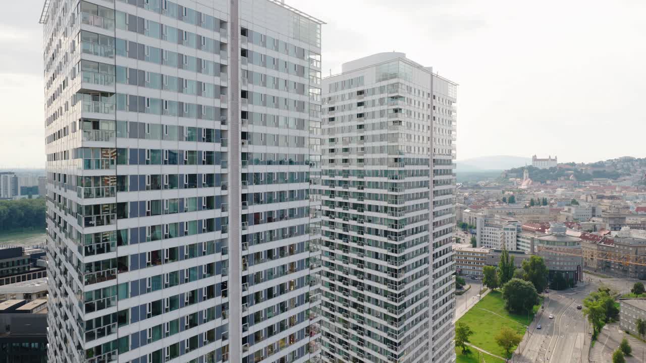 Drone view of tall residential towers in Bratislava, Slovakia, with glass facades and the historic city center, Danube River, and Bratislava Castle visible in the background