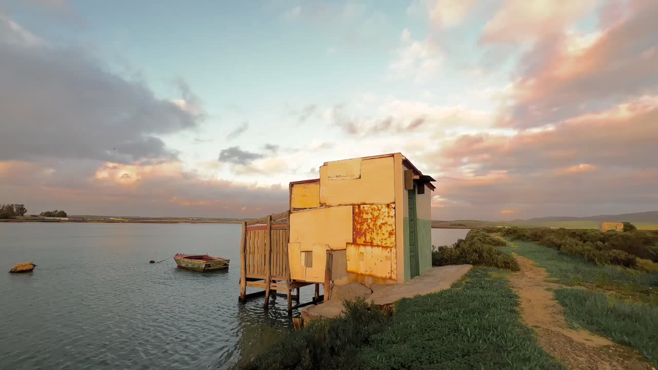 물 강변에 즉흥적으로 지어진 작은 집 위에 이동하는 구름의 시간 경과, 물 표면에 떠 있는 시 보트