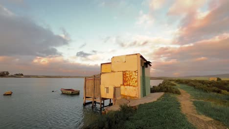 time-lapse of moving clouds over improvised built small house on water river bank, fishing boats floating on water surface