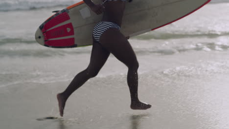 mujer corriendo con una tabla de surf en la playa