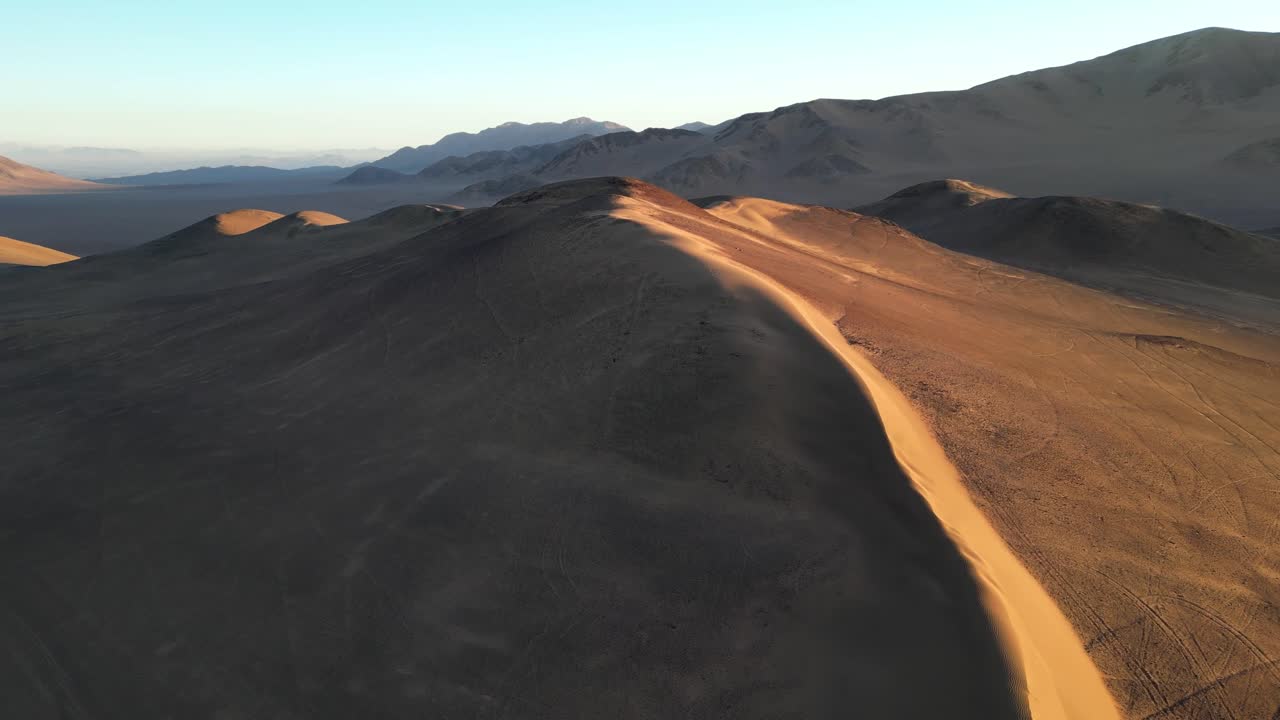 Drone perspective of ochre-colored dunes, with long shadows creating striking natural patterns across the Atacama