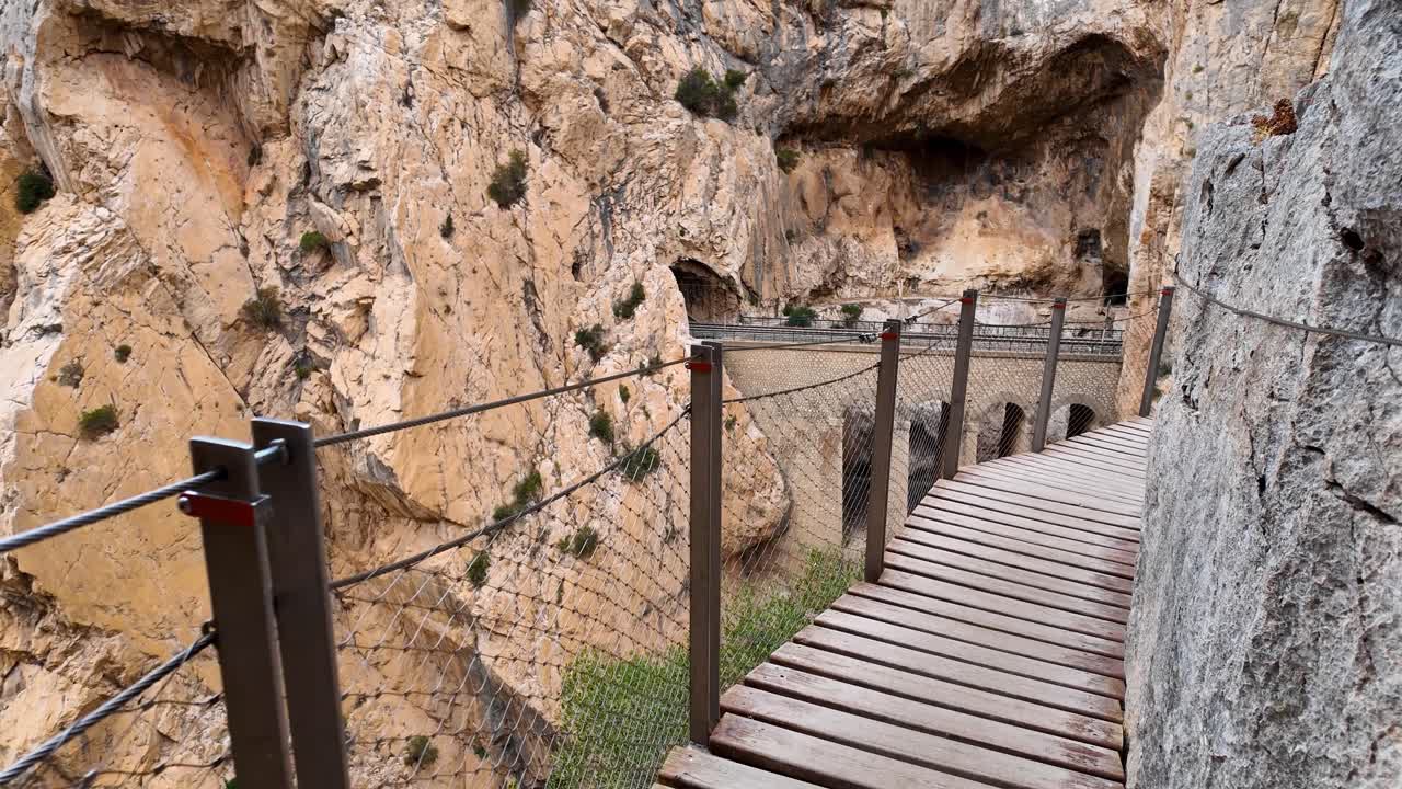 Malaga'daki Caminito del Rey'in ahşap yürüyüş yollarında el kamerası POV ile ilerlerken dar uçurum patikaları, güvenlik işaretleri ve kanyon vadisi manzarası ortaya çıkıyor.