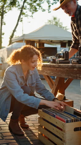 woman browsing records at an outdoor flea market with vintage cameras