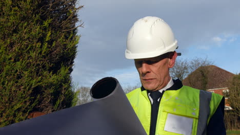 An-architect-looking-at-plans-of-a-building-on-a-construction-site-in-a-residential-street-with-traffic-on-the-road-in-the-background