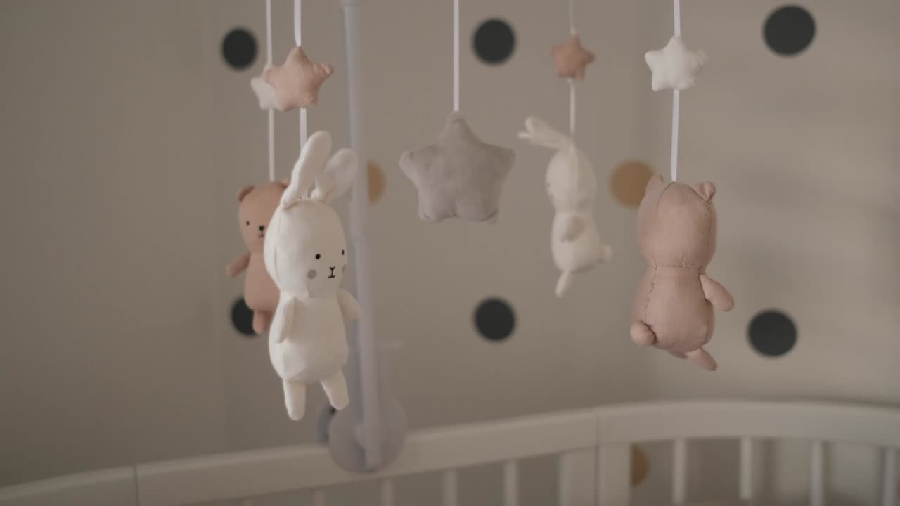 Cute stuffed baby animals rotating above white wooden crib in nursery