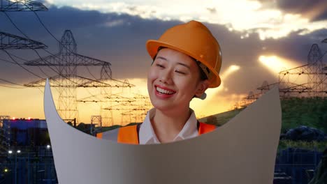 close-up de ingeniera asiática con casco de seguridad mirando el plan en sus manos mientras está de pie cerca de la torre de alto voltaje
