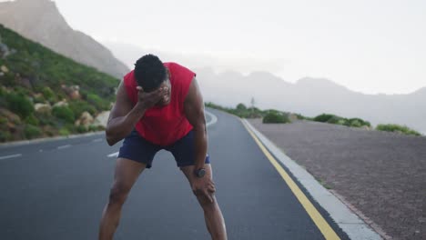 hombre afroamericano cansado tomando un descanso de correr en la carretera