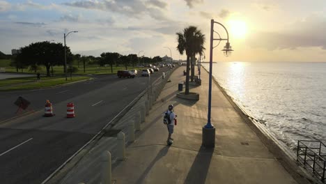 drone following skateboarder riding on electronic skateboard during sunset along lake pontchartrain. - aerial, rear