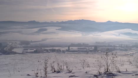 Panning-across-wide-open-winter-landscape-with-mountain-backdrop-and-road