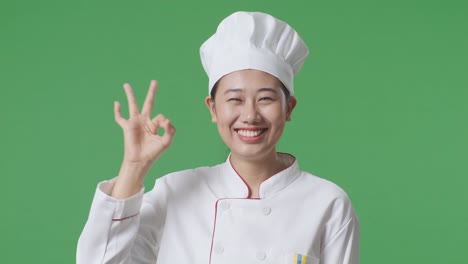 Close Up Of Asian Woman Chef Smiling And Showing Okay Gesture To Camera While Standing In The Green Screen Background Studio