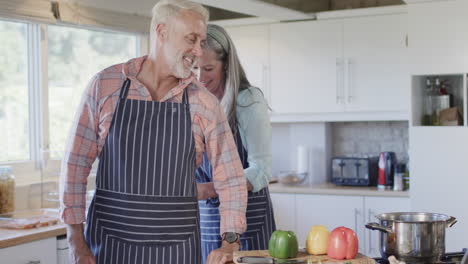 Pareja-Caucásica-De-Mediana-Edad-Poniendo-Delantal,-Cocinando-En-La-Cocina-De-Casa,-Cámara-Lenta