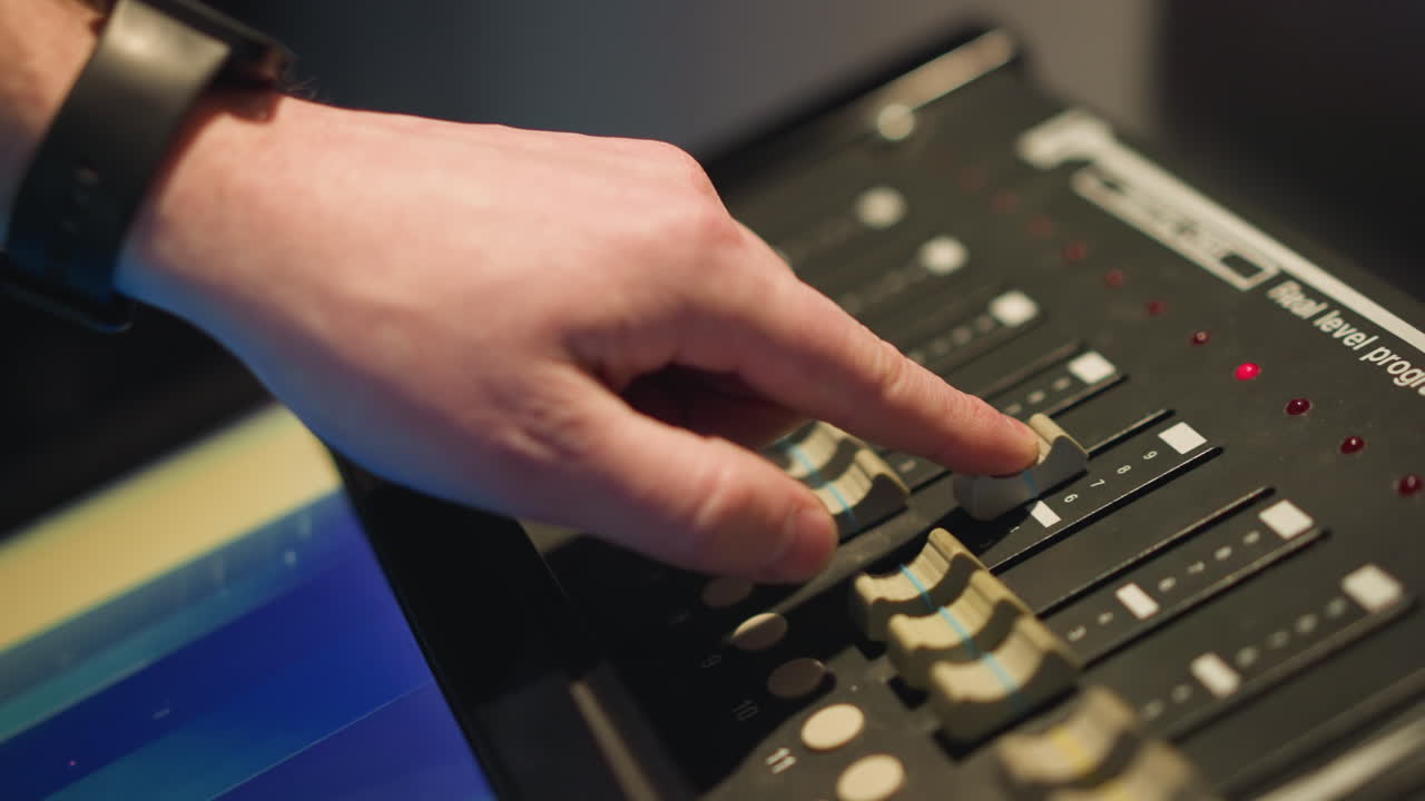 Close-up of hand adjusting fader on professional lighting control panel, fine-tuning levels, managing lighting settings for studio or stage, working with control buttons and display interface