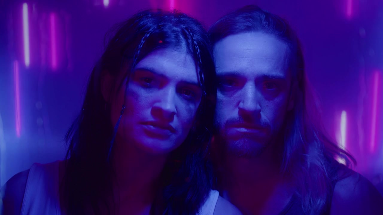 Giovane coppia in posa per la fotocamera sotto una luce al neon blu e viola