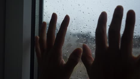 two hands against a window during a rainy day