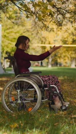 positive adult woman with spinal cord injury in wheelchair and preschooler girl play throwing autumn leaves upward. active family recreation during rehabilitation