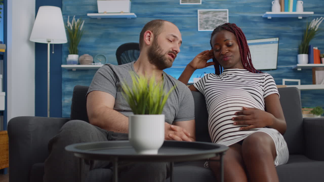 Interracial couple expecting child and bonding on couch