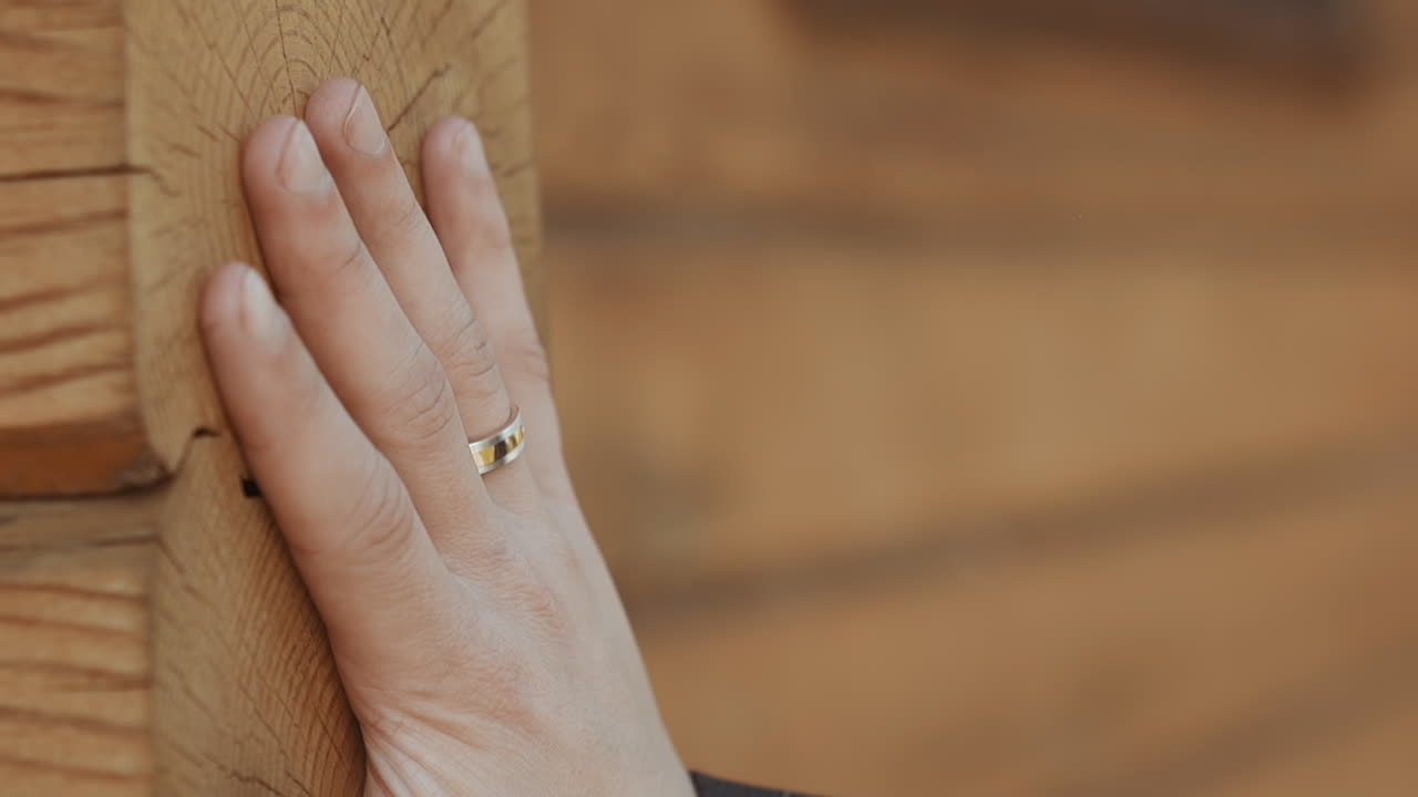Gentleman with wedding ring touches natural log wall