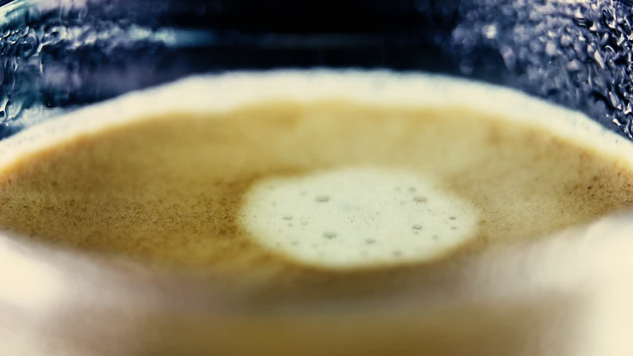 Closeup Drop of coffee falls into the filled Cup ripples in froth - abstract macro slow motion