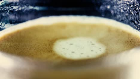 closeup drop of coffee falls into the filled cup ripples in froth - abstract macro slow motion