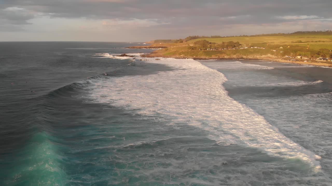 Surfaři čekají na perfektní vlnu a vlny se valí na pláž Ho'okipa na Maui na Havaji při západu slunce