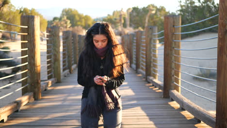 Una-Linda-Chica-Arrodillada-En-El-Suelo-Y-Leyendo-Un-Mensaje-De-Texto-En-Su-Smartphone-Con-Una-Mirada-Seria-Al-Atardecer-En-El-Desierto