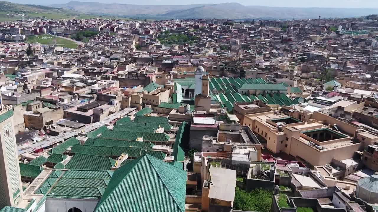 Comprehensive drone shot of the world's oldest university, Al-Qarawiyyin. Captures the iconic green roofs, the main minaret, and the surrounding ancient medina set against the Fez hills