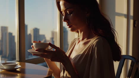 woman enjoying coffee/tea at a window with a city view