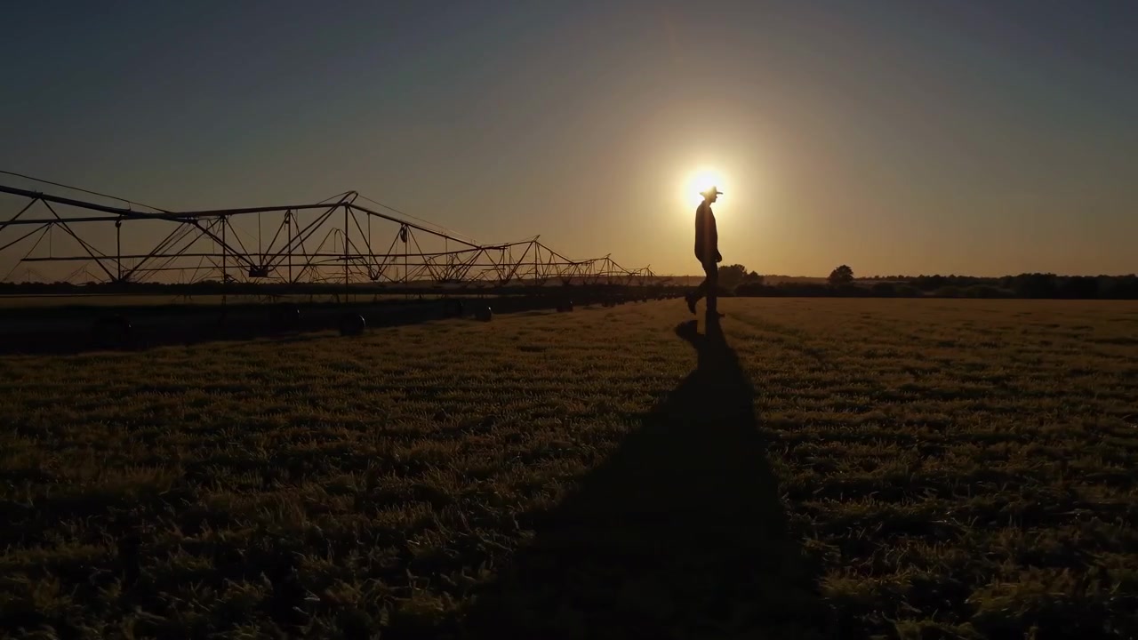 Contadino che cammina attraverso un campo al tramonto con sistema di irrigazione