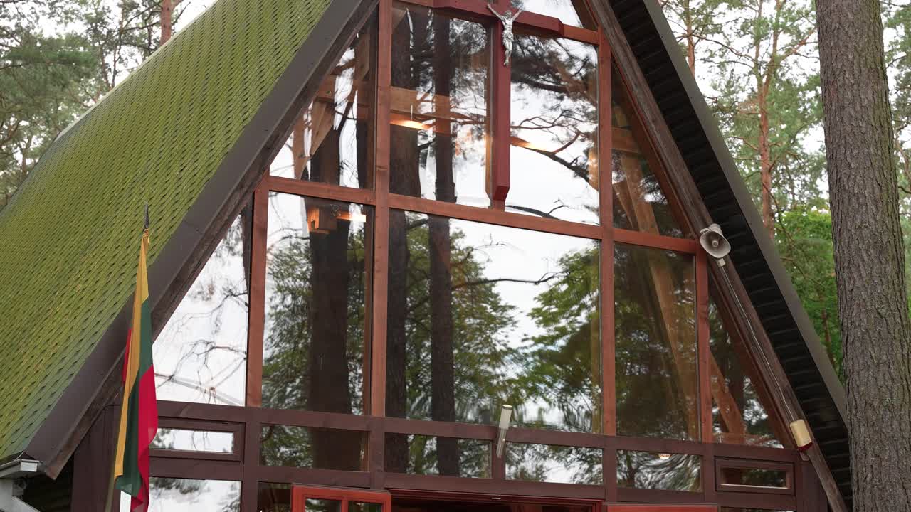 Close-up of St. Anne’s Chapel in Kačerginė, Lithuania, showcasing the wooden crucifix behind a large glass facade, surrounded by serene forest and nature