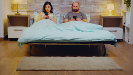 bored young couple in pajamas using smartphone