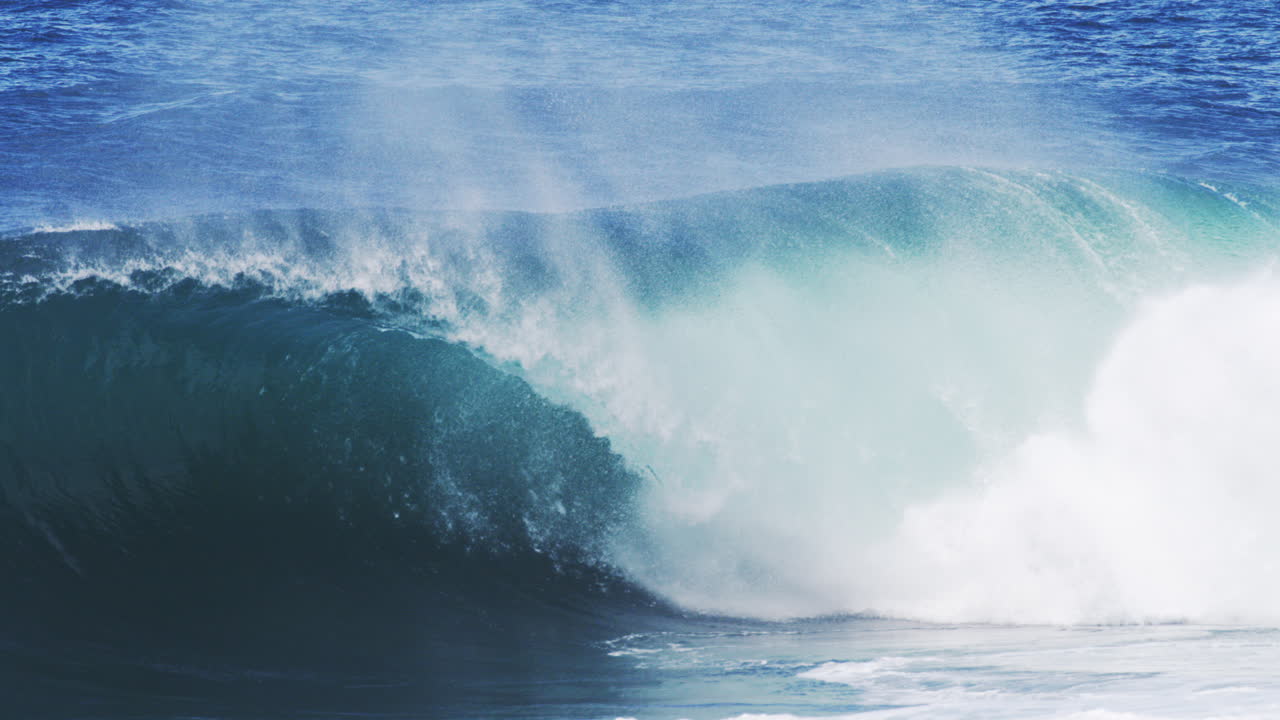 Towering wave breaks with thick foam and mist rising into the air in slow motion