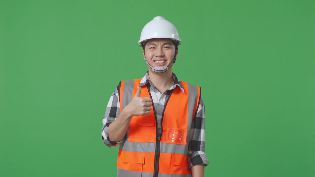 Asian Male Engineer With Safety Helmet Smiling And Showing Thumbs Up Gesture To The Camera While Standing In The Green Screen Background Studio