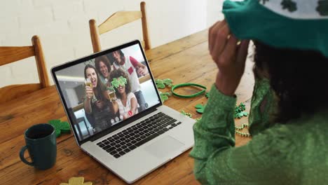 mujer caucásica en llamada de video portátil celebrando el día de san patricio con amigos