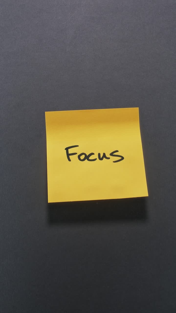 Hands posting Focus sticky note on dark wall, focusing on productivity